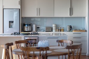 A modern kitchen with a central island, wooden chairs, and a stainless steel refrigerator. - Ocean View Apartment near V&A Waterfront (Cape Town)