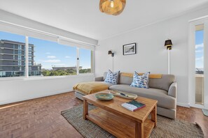 A modern living room with a large window, a sofa, a coffee table, and a lamp. - Ocean View Apartment near V&A Waterfront (Cape Town)