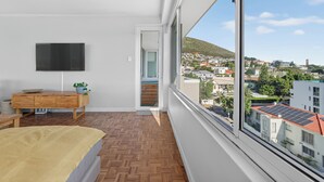 A bedroom with a large window, a bed, a TV, and a wooden dresser. - Ocean View Apartment near V&A Waterfront (Cape Town)
