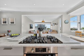 A modern kitchen with a central island, built-in appliances, and a view to the living area. - Ocean View Apartment near V&A Waterfront (Cape Town)