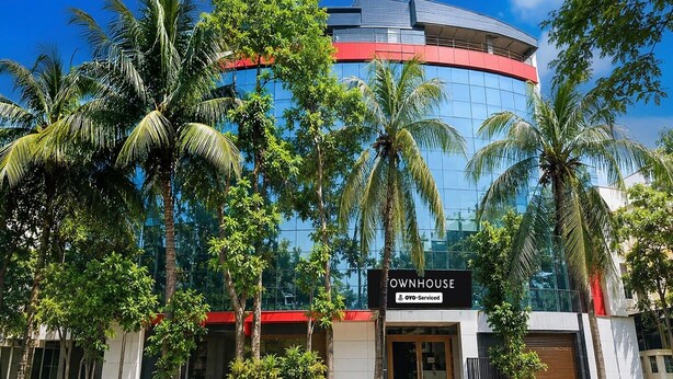 Um edifício moderno com fachada curva, palmeiras e uma placa com a inscrição 'OWNHOUSE OYO-Serviced'.