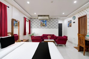 A hotel room with a bed, a red sofa set, a small table, a mirror, and a clock on the wall.