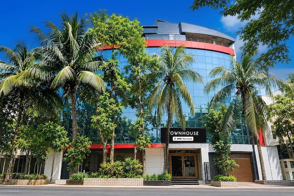 A modern building with a curved facade, palm trees, and a sign that reads 'OWNHOUSE OYO-Serviced'.