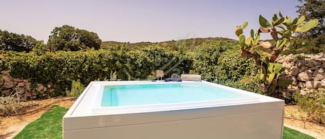 A rectangular pool with a white border, surrounded by green grass and a stone wall.