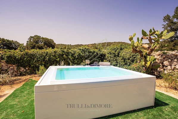 A rectangular pool with a white border, surrounded by green grass and a stone wall.
