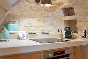 Une cuisine avec un mur en pierre, une bouilloire de couleur turquoise, une machine à café et une balance numérique.
