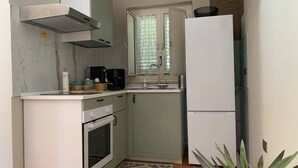 Eine kleine Küche mit weißem Arbeitsplatz, einem Herd, einer Spüle und einem Kühlschrank.