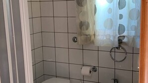 Ein Badezimmer mit Toilette, Bidet und Waschbecken, gefliestem Boden und einem Vorhang mit Punkte-Muster.