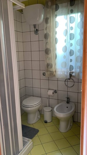 A bathroom with a toilet, bidet, and sink, tiled floor, and a curtain with a polka dot pattern. - Through the Alleys of Girgenti (Agrigento)