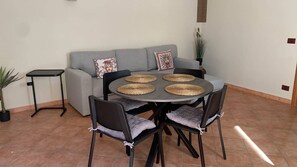 A dining area with a round table, four chairs, and a grey sofa with decorative pillows. - Through the Alleys of Girgenti (Agrigento)
