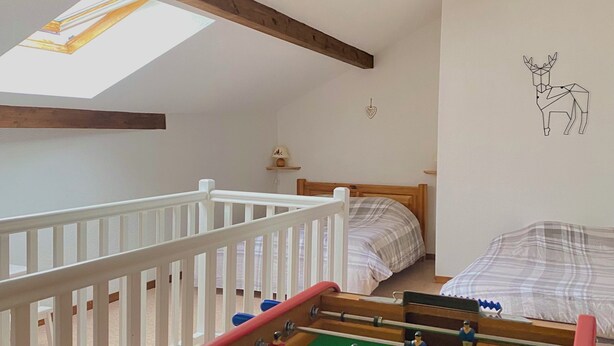 A room with a foosball table, a bed, a crib, and a skylight.