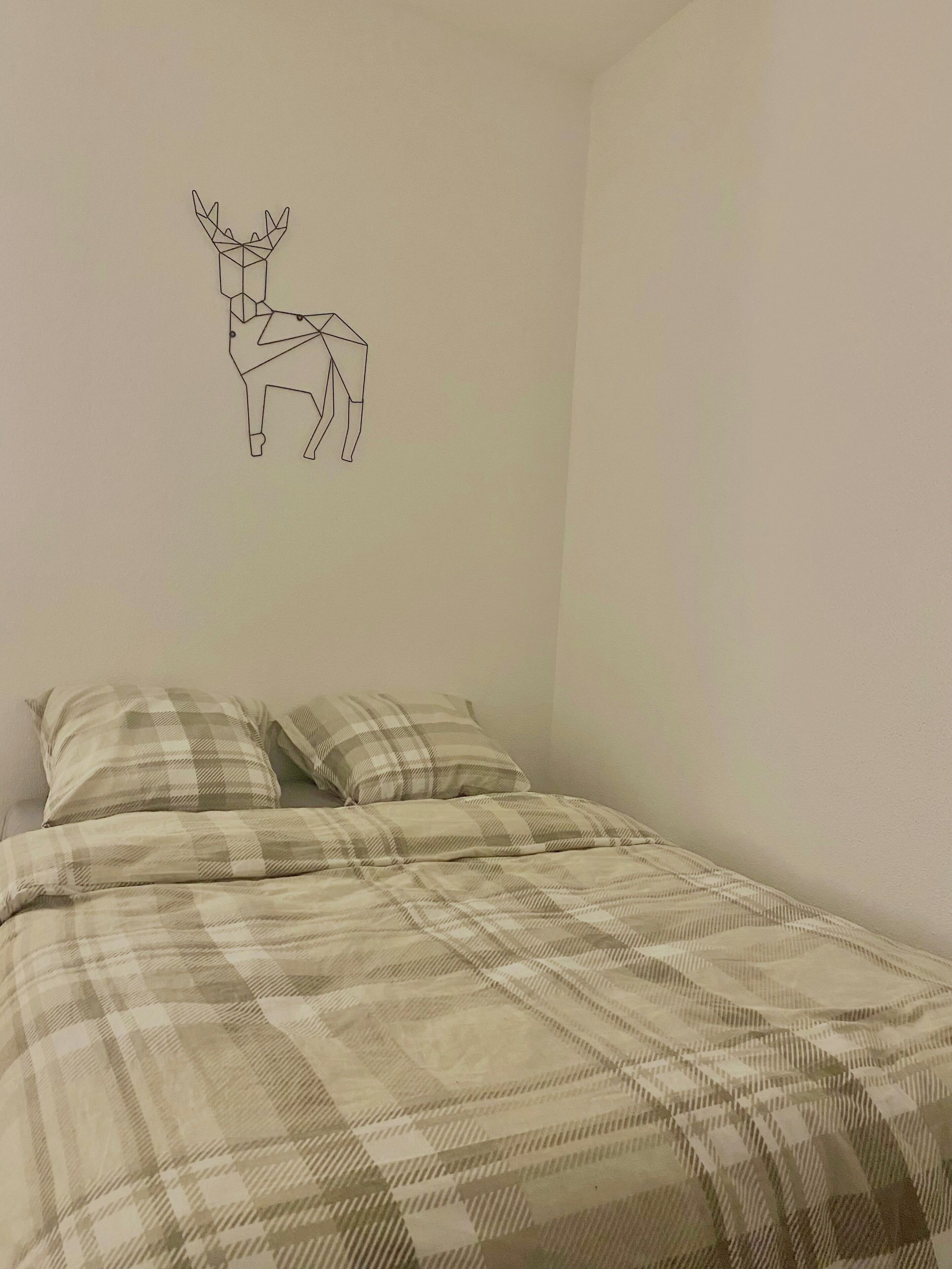 Ein Schlafzimmer mit einem Bett, zwei Kissen und einer Wandsticker-Darstellung eines Rehs.