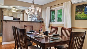 Un comedor con una mesa de madera dispuesta para cuatro personas, una araña y vistas del exterior a través de una ventana.