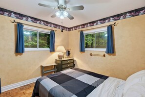 Quarto com cama, mesa de cabeceira, luminária, espelho e ventilador de teto.