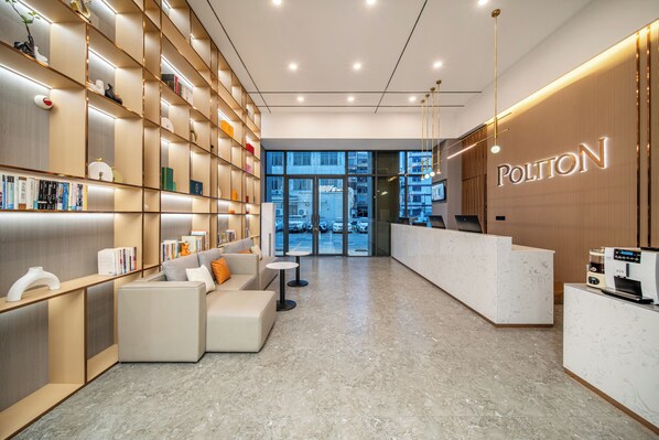 A modern hotel lobby with a reception desk, seating area, and a bookshelf filled with books and decorative items.