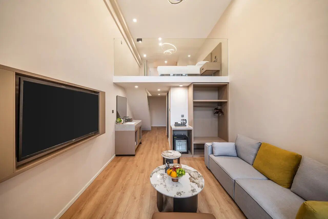 A compact living space with a sofa, a dining table with fruit, a TV, and a kitchenette.