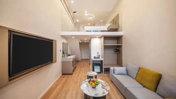 Un espace de vie compact comprenant un canapé, une table à manger avec des fruits, un téléviseur et une petite cuisine.