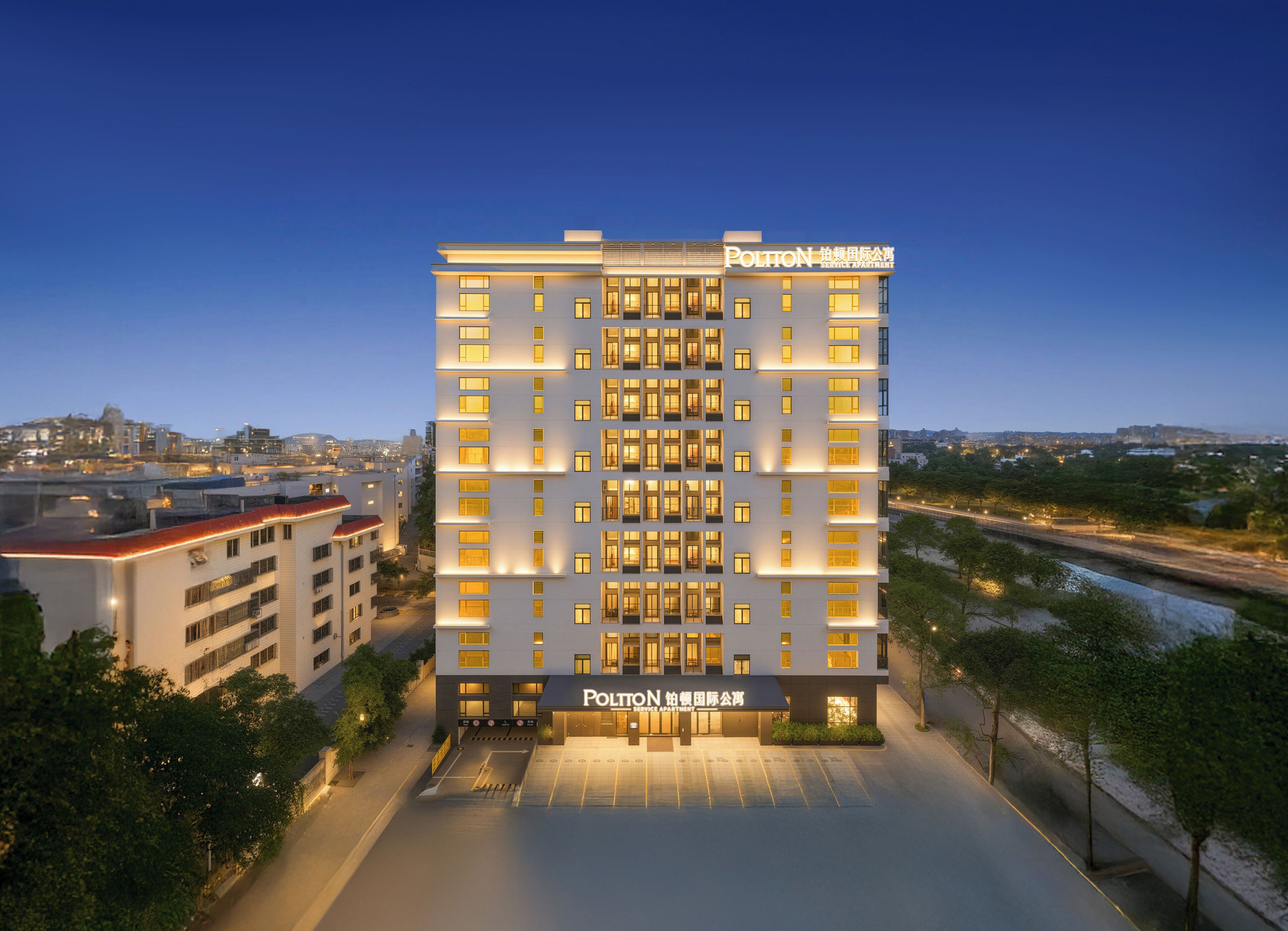 A multi-story hotel with a service apartment section, featuring a modern facade and illuminated windows.