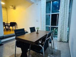 Un comedor con una mesa y sillas de madera, una planta en maceta y vistas a través de una ventana con cortinas.