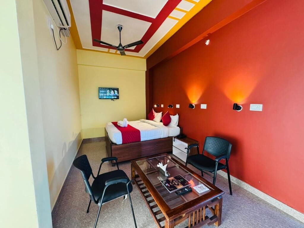 A hotel room with a bed, a desk, two chairs, a ceiling fan, and a wall-mounted light fixture.