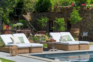A poolside area with wicker lounge chairs and a stone wall backdrop. - Villa Maionchi: Timeless Tuscan Elegance & Luxury (Capannori)