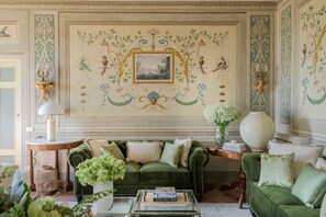Ein Zimmer mit einem grünen Sofa, einer weißen Vase mit Blumen und einem gerahmten Bild an der Wand.