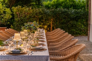 A long dining table set with wicker chairs, glassware, and a centerpiece. - Villa Maionchi: Timeless Tuscan Elegance & Luxury (Capannori)