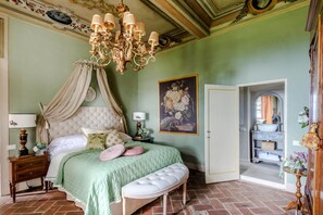 A bedroom with a four-poster bed, a chandelier, a painting, and a bathroom visible through an open door. - Villa Maionchi: Timeless Tuscan Elegance & Luxury (Capannori)