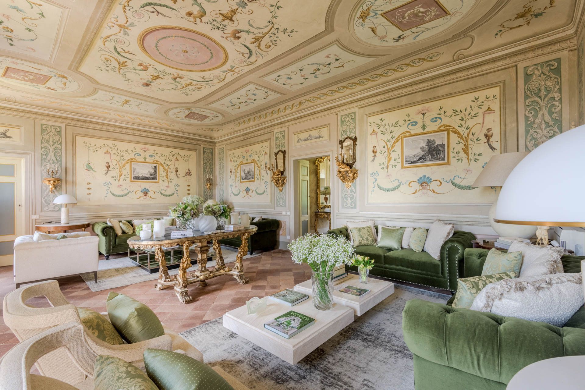Une chambre luxueuse ornée de fresques complexes au plafond, avec un canapé vert et une table basse en marbre.