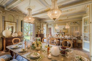 A dining room with ornate chandeliers, a large dining table set for a meal, and a view of the outdoors through a doorway. - Villa Maionchi: Timeless Tuscan Elegance & Luxury (Capannori)