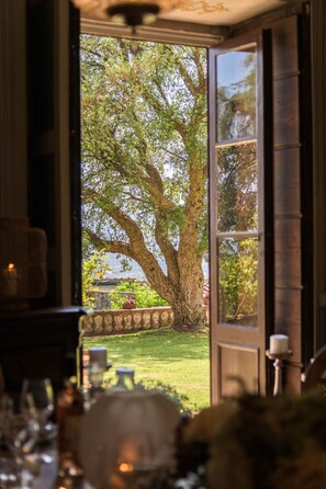 A view through an open door to a tree-lined outdoor area with a stone wall and a grassy lawn. - Villa Maionchi: Timeless Tuscan Elegance & Luxury (Capannori)