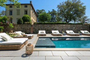 A poolside area with lounge chairs, a stone wall, and a building in the background. - Villa Maionchi: Timeless Tuscan Elegance & Luxury (Capannori)