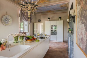 A modern kitchen with a central island, a chandelier, and a decorative ceiling. - Villa Maionchi: Timeless Tuscan Elegance & Luxury (Capannori)
