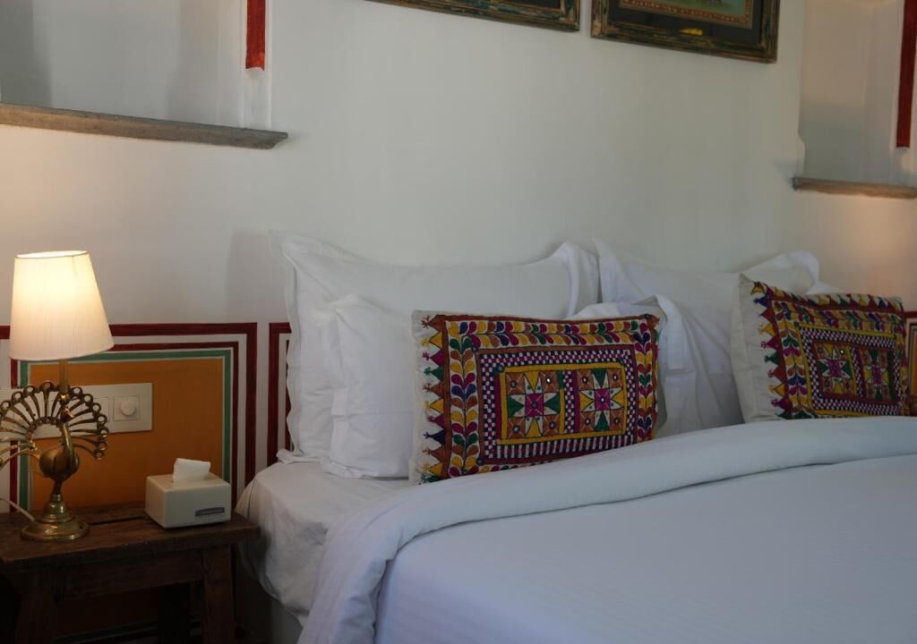A hotel room with a bed, a bedside lamp, a tissue box, and a decorative pillow.