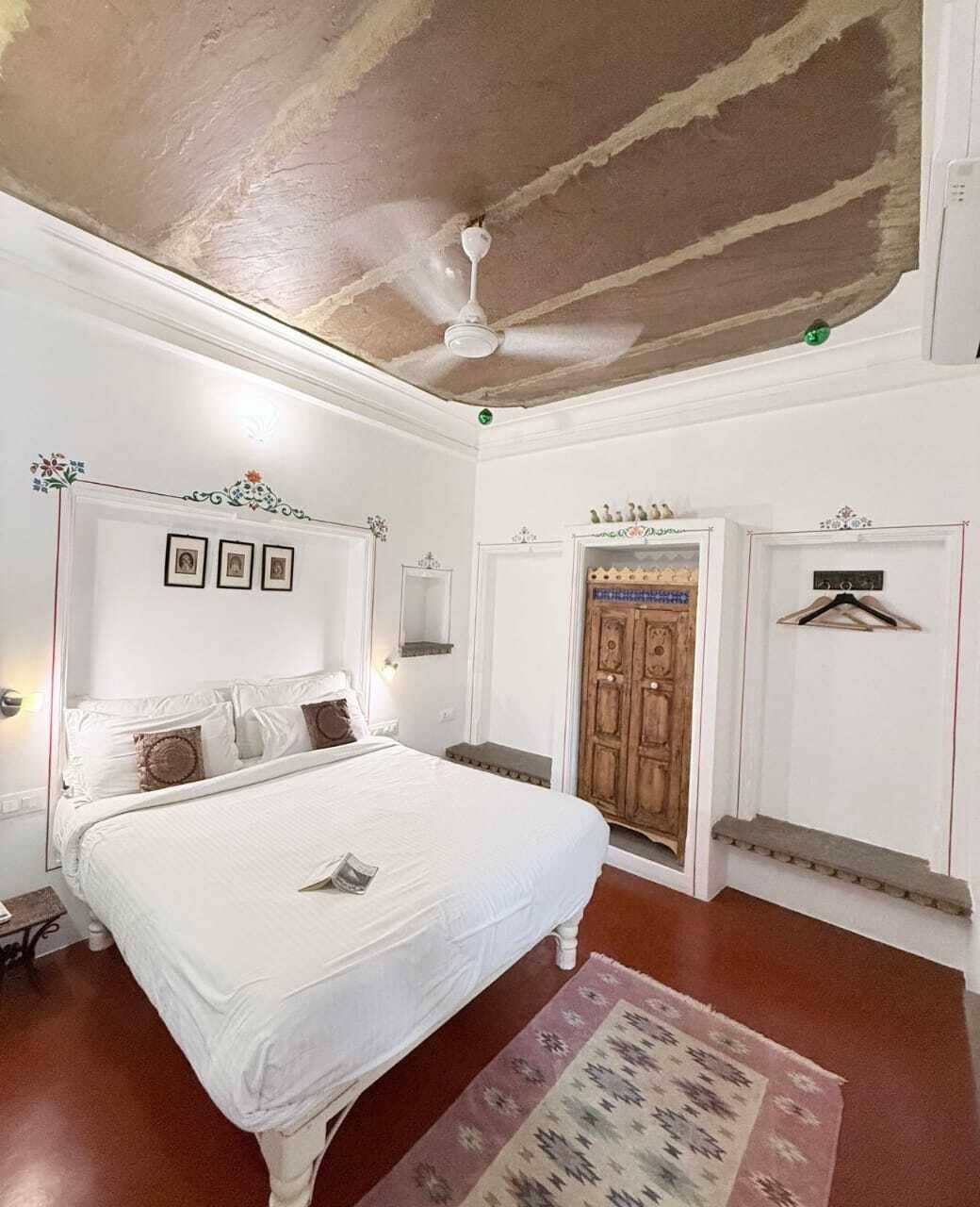 A bedroom with a bed, a ceiling fan, a wooden door, and a small table.