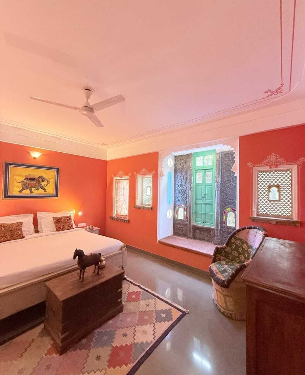 A bedroom with a bed, a ceiling fan, a window with a green door, and a decorative chair.