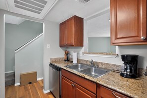 A compact kitchen with wooden cabinets, a stainless steel sink, a coffee maker, and a dishwasher. - Regency Place | Modern Comfort, 2BR Home (Beaumont)