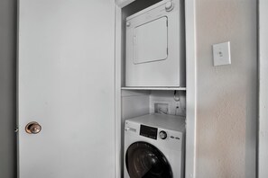 A laundry room with a front-loading washing machine and a top-loading dryer. - Regency Place | Modern Comfort, 2BR Home (Beaumont)