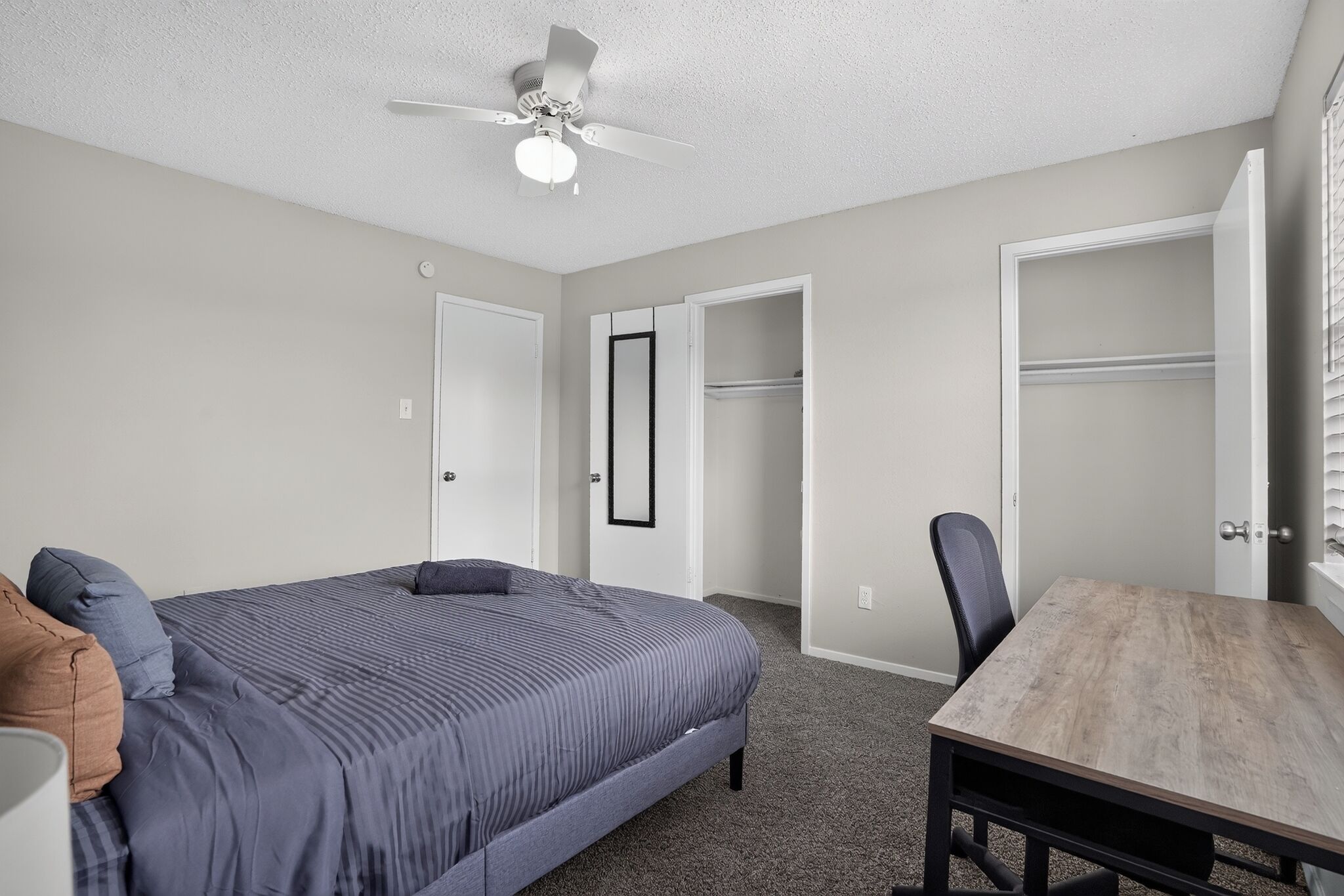 A bedroom with a bed, a desk, a chair, a wardrobe, and a ceiling fan.