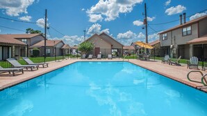 Ein Pool mit Liegestühlen und einer überdachten Liegefläche, umgeben von Häusern.