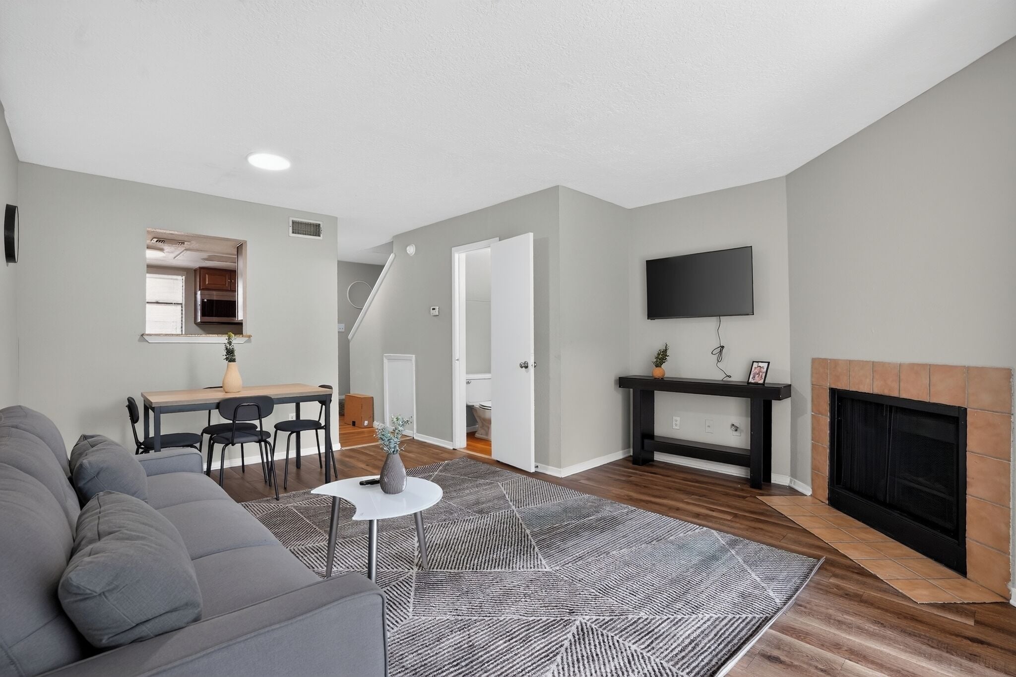 A modern living room with a gray sofa, a dining area with a table and chairs, a fireplace, and a TV mounted on the wall.