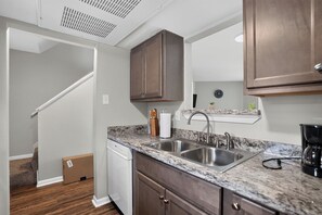 A kitchen with a double sink, wooden cabinets, a marble countertop, and a coffee maker. - Regency Place | Fully Furnished 2BR Home (Beaumont)