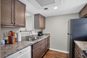 A kitchen with wooden cabinets, a stainless steel sink, a marble countertop, and a black refrigerator. - Regency Place | Fully Furnished 2BR Home (Beaumont)
