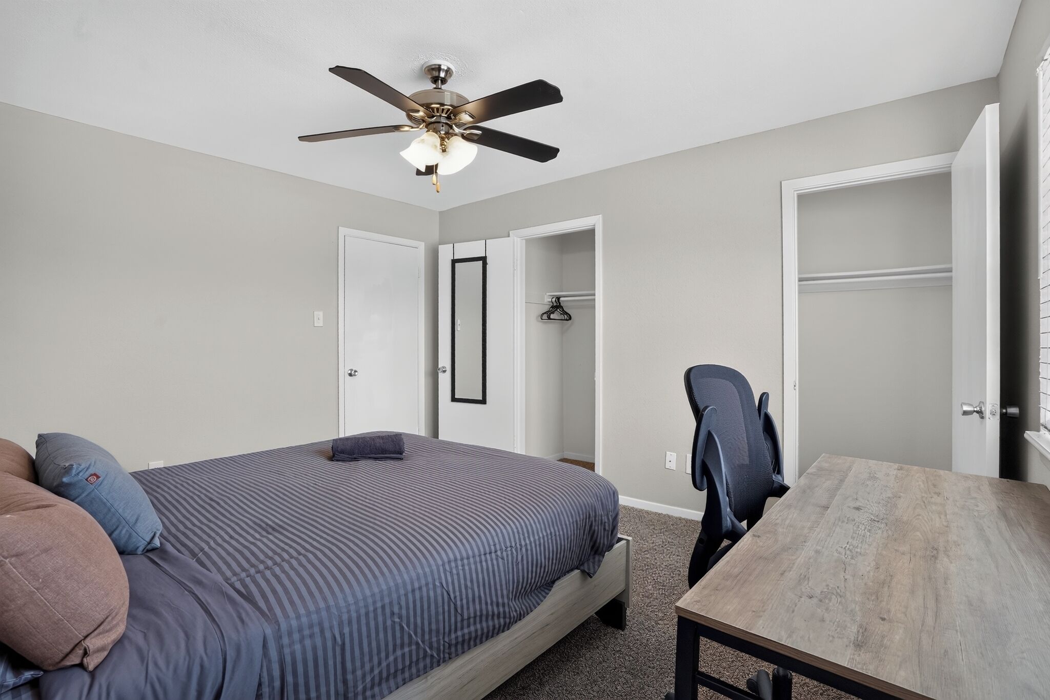 Une chambre à coucher comprenant un lit, un bureau, une chaise, une armoire et un ventilateur de plafond.