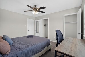 A bedroom with a bed, a desk, a chair, a wardrobe, and a ceiling fan. - Regency Place | Cozy 2BR for Work & Rest (Beaumont)