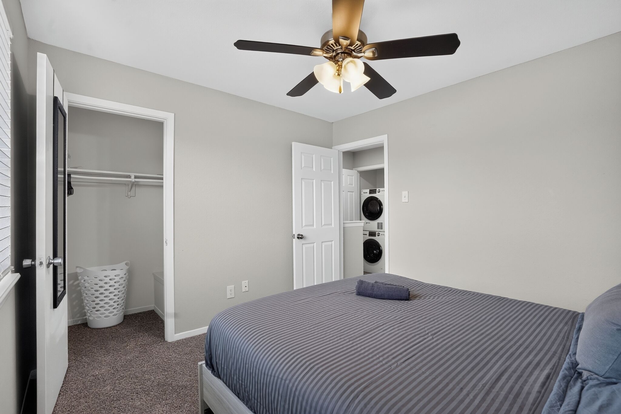 A bedroom with a bed, a ceiling fan, a washing machine, and a laundry basket.