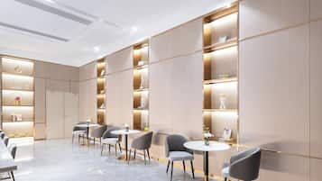 A modern interior with a row of tables and chairs, wooden panel walls, and built-in shelving with decorative items.