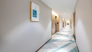 Een hotelgang met een kamerbreed tapijt, deuren en een abstract kunstwerk in een lijst aan de muur.