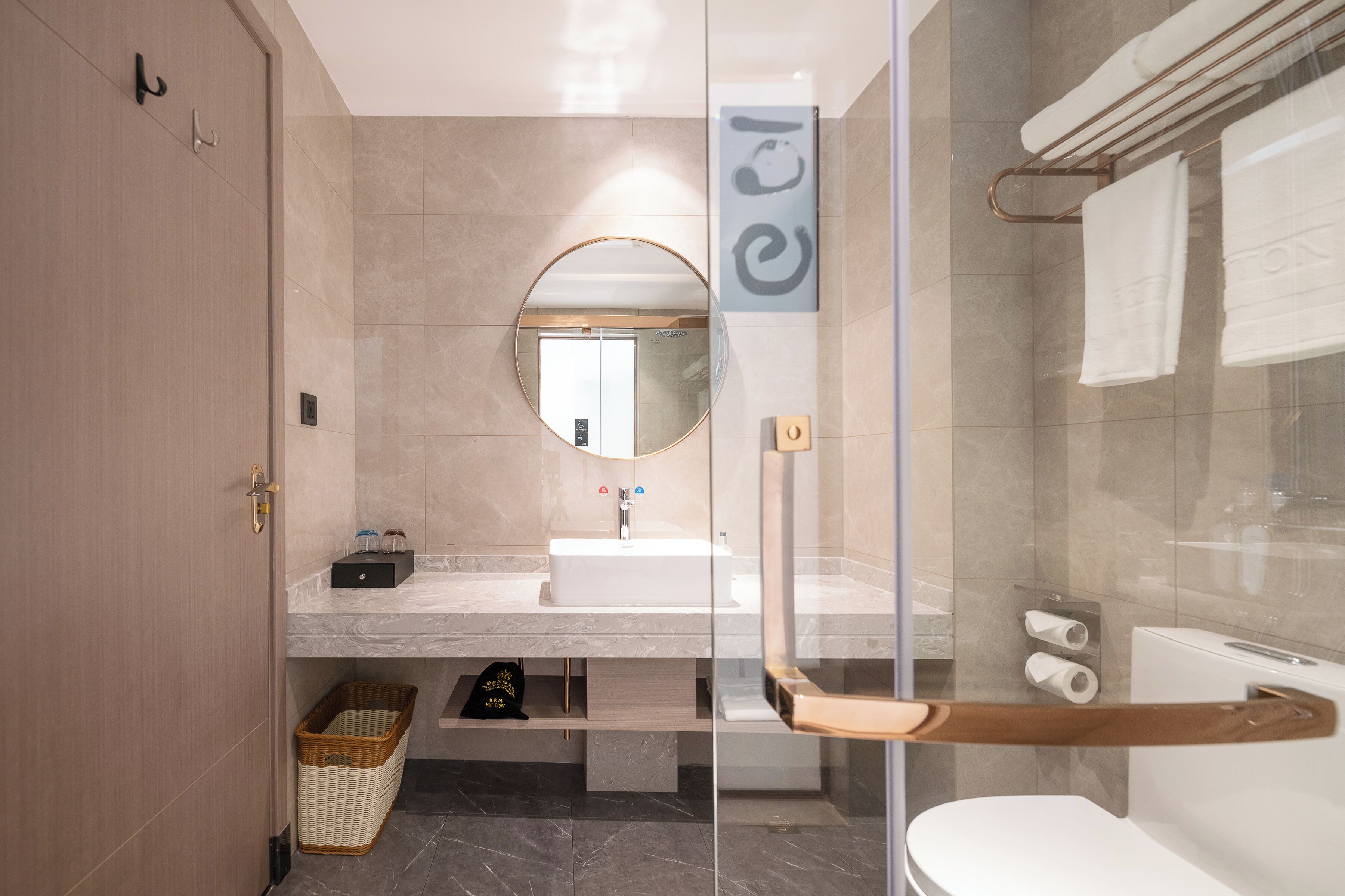 Un bagno moderno con cabina doccia in vetro, uno specchio rotondo, un lavandino bianco e un porta asciugamani.