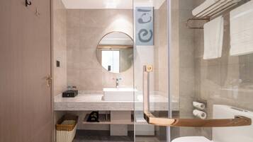 Un bagno moderno con cabina doccia in vetro, uno specchio rotondo, un lavandino bianco e un porta asciugamani.